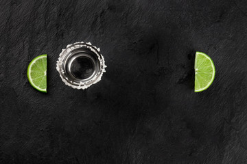 A photo of a tequila shot with lime slices forming a frame, shot from the top on a black background with copy space