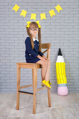 Cute school girl posing in studio shoot in school uniform dress and jacket on background of letters...