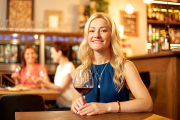 people, alcohol and lifestyle concept - happy woman drinking red wine at restaurant or bar