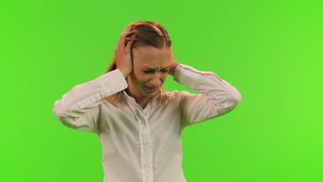A disturb woman puts an earmuffs to protect her ears from noise, relaxes and smiles, over a green screen.