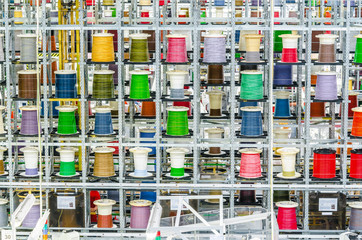 Large coils with colored electrical wires on huge shelves in an industrial plant. Manufacture of electrical wiring for cars. Employment in industry