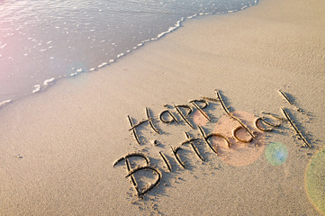 Happy Birthday! message handwritten in smooth sand with festive lens flare on the shore of an empty...