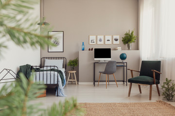 Forest inspiration in trendy teenager bedroom with vintage armchair, desk with computer and branches of spruce in glass vase