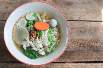 Thai noodle soup with chicken and fish ball, carrot, vegetable and coriander in a bowl on wooden table background with copy space.