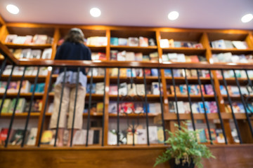 Blurred abstract background of bookshelves in book store, with a girl finding book in the store.