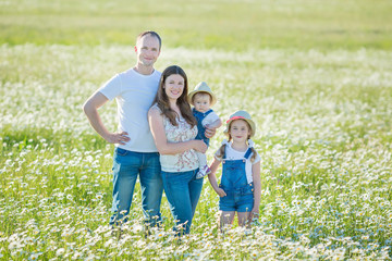 Fototapeta premium Young family in a field of flowers daises chamomile anjoy spa life happy together with cute faces in a village rustic motion
