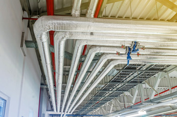 Metal pipes in thermal insulation winding on the ceiling of an industrial enterprise.