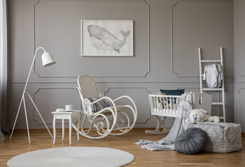 White rocking chair with pillow in the middle of cozy baby room interior with wooden cradle,...