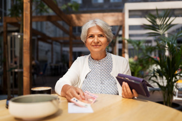old age, leisure, payment and finances concept - happy senior woman with wallet and money paying bill for coffee and dessert at street cafe