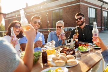 leisure and people concept - happy friends with drinks having barbecue party on rooftop