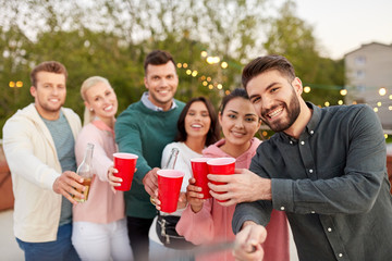 leisure and people concept - happy friends with drinks taking selfie at rooftop party in summer