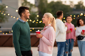 leisure, celebration and people concept - happy friends with drinks in party cups toasting at rooftop