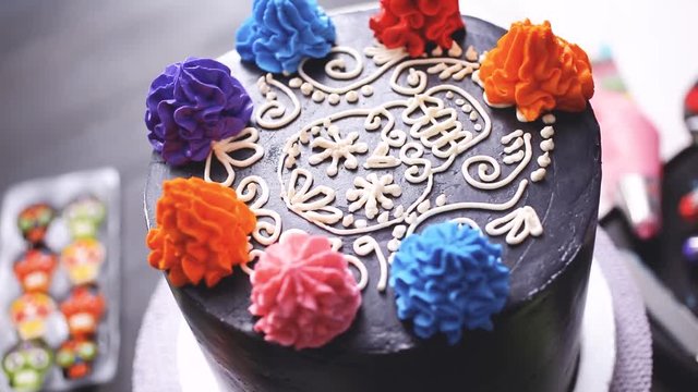 Baker piping colorful buttercream italian icing on a top of multilayer cake for Dia de los Muertos holiday.