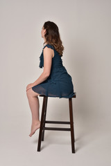 full length portrait of brunette girl wearing short blue dress.  on creamy studio background.