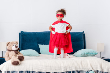 little african american kid in red superhero costume and mask with hands on hips standing on bed © LIGHTFIELD STUDIOS