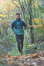 Young athlete with beard runs in the rain on a trail with technical clothing