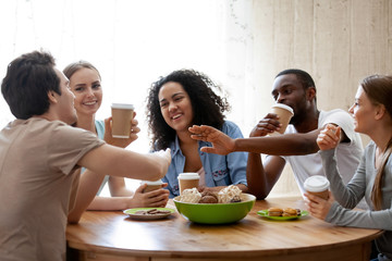 Diverse friends girls and guys sitting around table chatting having fun drink coffee in paper cups enjoy time together. Friendship between different race multinational young millennial people concept