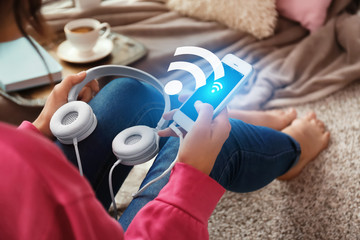 Woman with smartphone and headphones sitting on floor at home