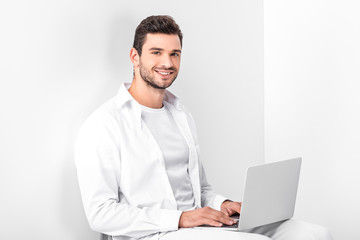 adult smiling handsome man in total white using laptop