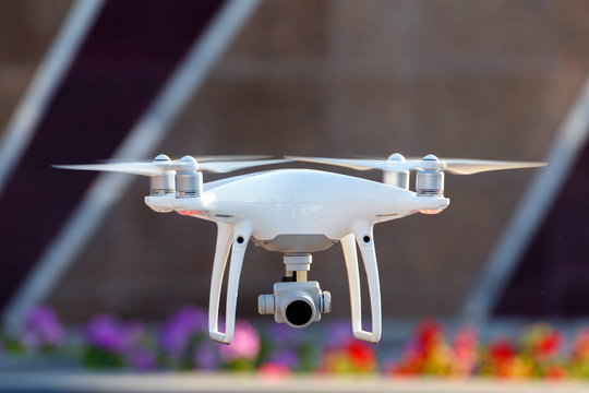 The white quadrocopter takes off over the sidewalk.