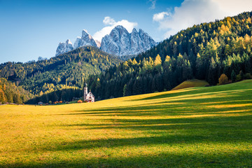 Fabulous view of Chiesetta di San Giovanni in Ranui church in front of the Geisler or Odle Dolomites Group. Colorful autumn sunset in Dolomite Alps, Italy, Europe. Traveling concept background.