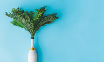 Champagne bottle with tropical green palm leaves on pastel blue background. Summer holiday concept...