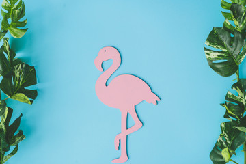 Pink flamingo shape with green tropical leaves on bright blue background. Summer tropical composition with copy space. Flat lay minimal. Summer Holiday layout.