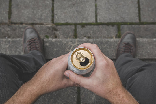 Young man's hands holding metallic can. Beer drinking. Suffering from life difficulties or psychological problems. Depressive atmosphere. Dark, gloomy thoughts. Social isolation. Top view. Close up.