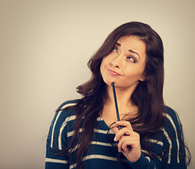 Confusion grimacing brunette woman thinking and looking up with question in eyes and pencil under the face in warm sweater. Toned closup portrait