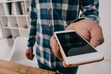 cropped shot of man showing smartphone with blank screen at wooden tabletop