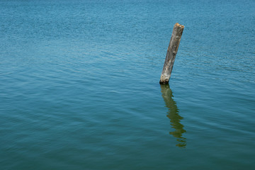 Old wonky wooden pole standing in sea water.