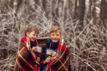 Children drink hot chocolate under warm blanket in winter forest. Christmas vacation.
