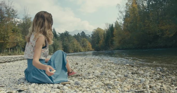 Young woman throwing rocks into the river