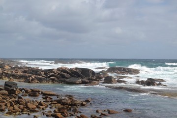 Fototapeta na wymiar ocean waves crashing on rocks with a cloudy sky