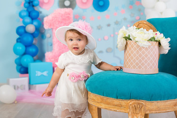 Fototapeta premium Cute little baby girl with big blue eyes wearing tutu hat and flower in her hair posing sitting in studio decorations with number one celebrating her birthday