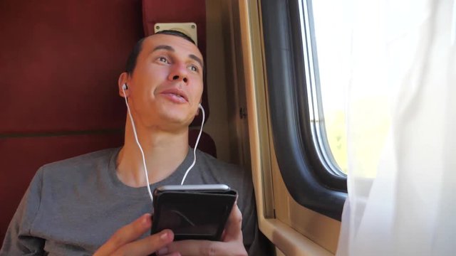 man listening to the music on the train rail car coupe compartment travel. slow motion video. lifestyle man with a smartphone at the window of a train in a car travel internet social media web. man