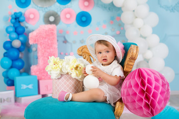 Fototapeta na wymiar Cute little baby girl with big blue eyes wearing tutu hat and flower in her hair posing sitting in studio decorations with number one celebrating her birthday