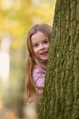 Fototapeta premium Kleines Mädchen schaut lachend hinter einem Baum hervor