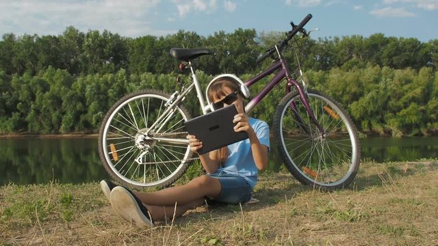A child plays video games. Little girl on nature with a tablet. Cyclist on the Internet.