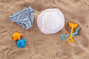 Fototapeta na wymiar Beach accessories for kids flat lay. Top view of children beach items on sand. Baby plastic scoop, rake, hat and blue children's panties. Water toys. Family summer vacation in tropical resort.