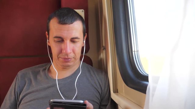 man listening to the music on the train journey rail car coupe compartment travel. slow motion video. man with a smartphone at the window of a train in a car travel internet social media web. man