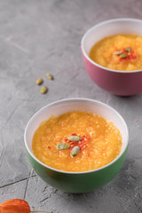 Pumpkin soup puree in ceramic bowls on a gray textured background.