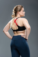 Fototapeta na wymiar back view of young overweight woman in sportswear standing with hands on waist isolated on grey