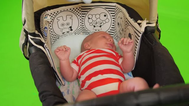 A cute Newborn baby boy moves in his stroller happily over a green screen.
