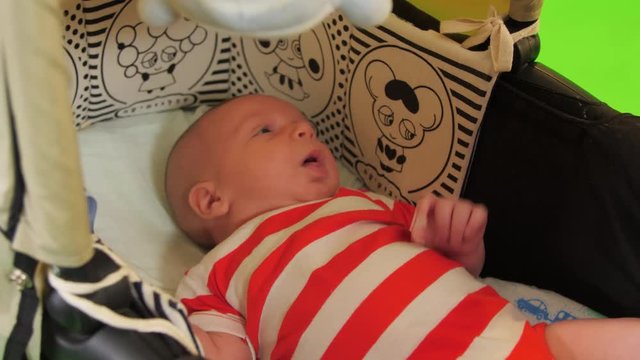 A cute Newborn baby boy laughs in his stroller happily over a green screen.