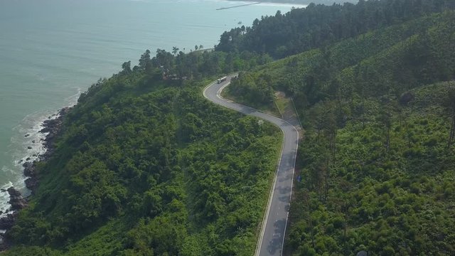 AERIAL: Large truck drives down the scenic coastal road in lush green Vietnam. Flying above tropical forest covering the mountain in rural Asia. Spectacular shot from above of famous Hai Van pass.