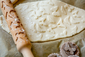 Rolling pin with a pattern on a wooden decorated table covered with baked flour. Rolled dough with a pattern and cookie of various shapes. Spring theme. Biscuit cooking background, close-up