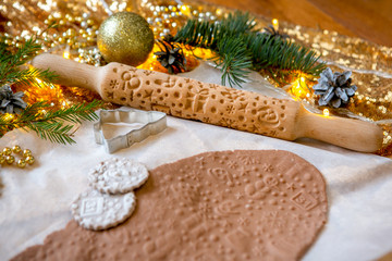 Rolling pin with a pattern on a wooden decorated table covered with baked flour. Rolled dough with a pattern and cookie of various shapes. New year theme. Biscuit cooking background, close-up