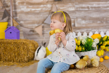 Cute little girl in jeans and white blouse playing hide and seek with a chicken sitting at a haystack close to yellow eggs and wooden background. The concept of children with animals. Studio