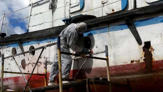 Workers tear off paint on metal in repairs process at shipyard.